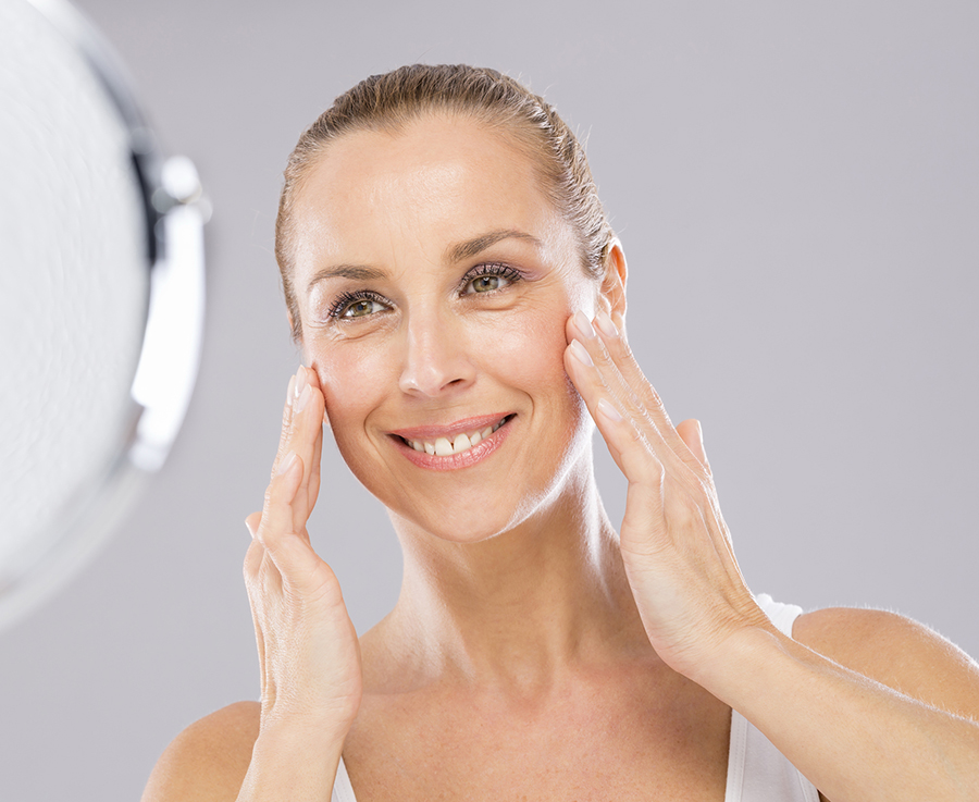 Middle aged woman with care and tenderness face skin looking to the mirror.