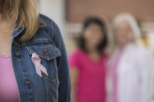 Unrecognizable woman wears a breast cancer awareness ribbon on her denim jacket. She is seen from the neck down.